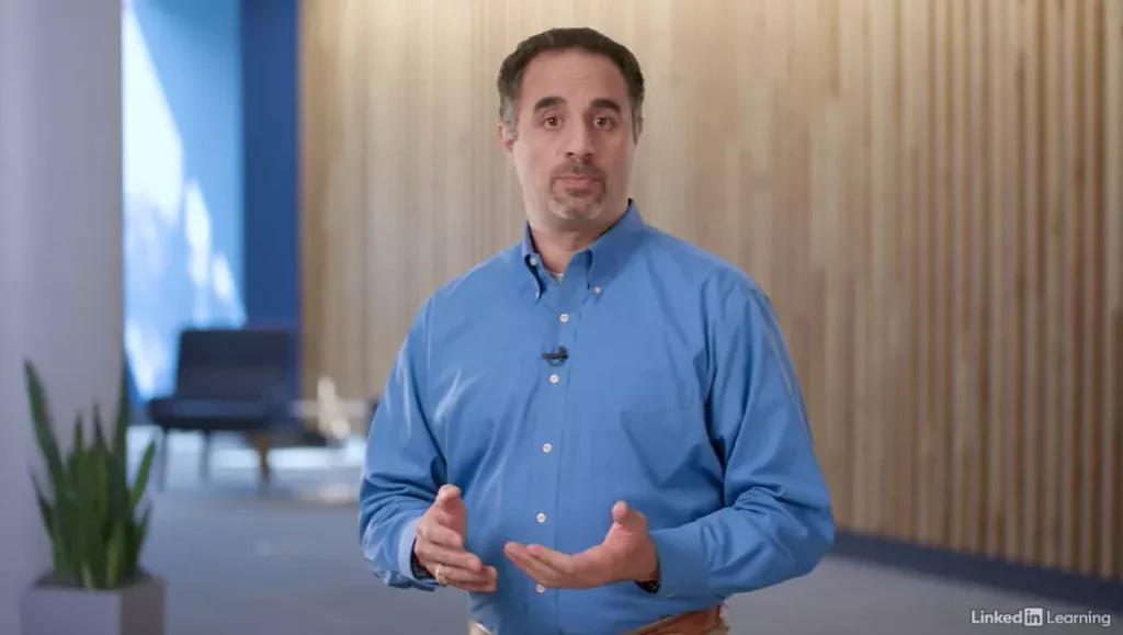 A man in a blue shirt standing infront of a wooden wall