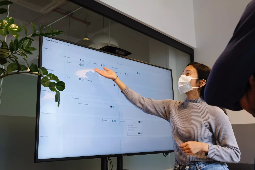 A girl with a mask  is presenting something on a monitor