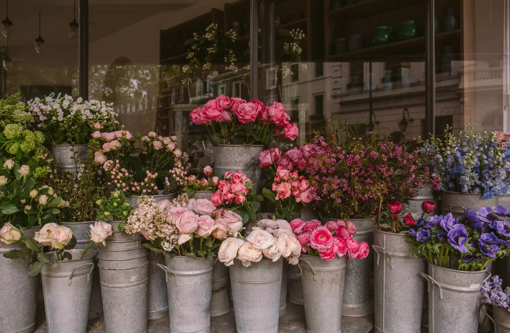 White and pink flowers arranged in grey buckets and displayed infront of a shop for selling