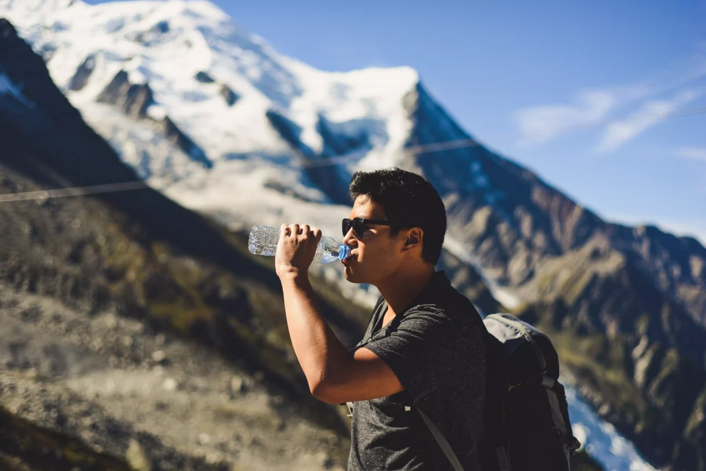 A guy hiking, making a break and drinking water