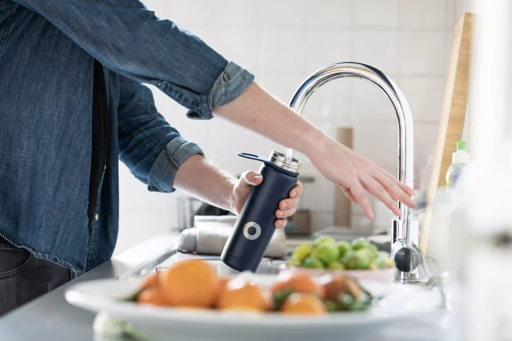 A man siping water from the sink, in a insulated water bottle