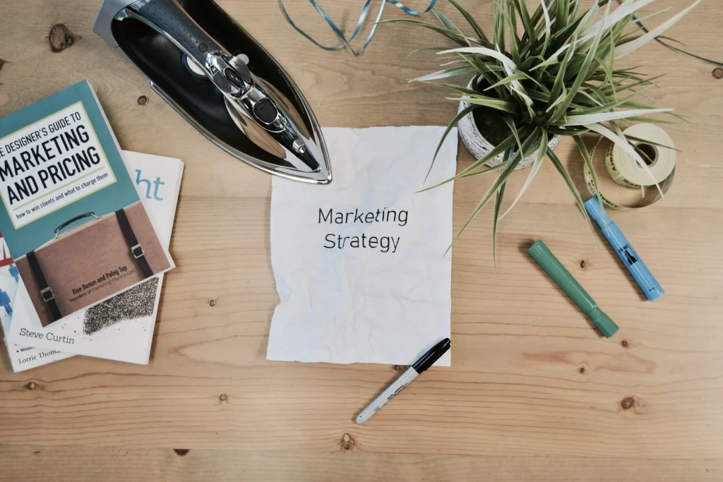 A table seen from an helicopter perspective. There are plants, pencils and a piece of paper that says marketing strategy