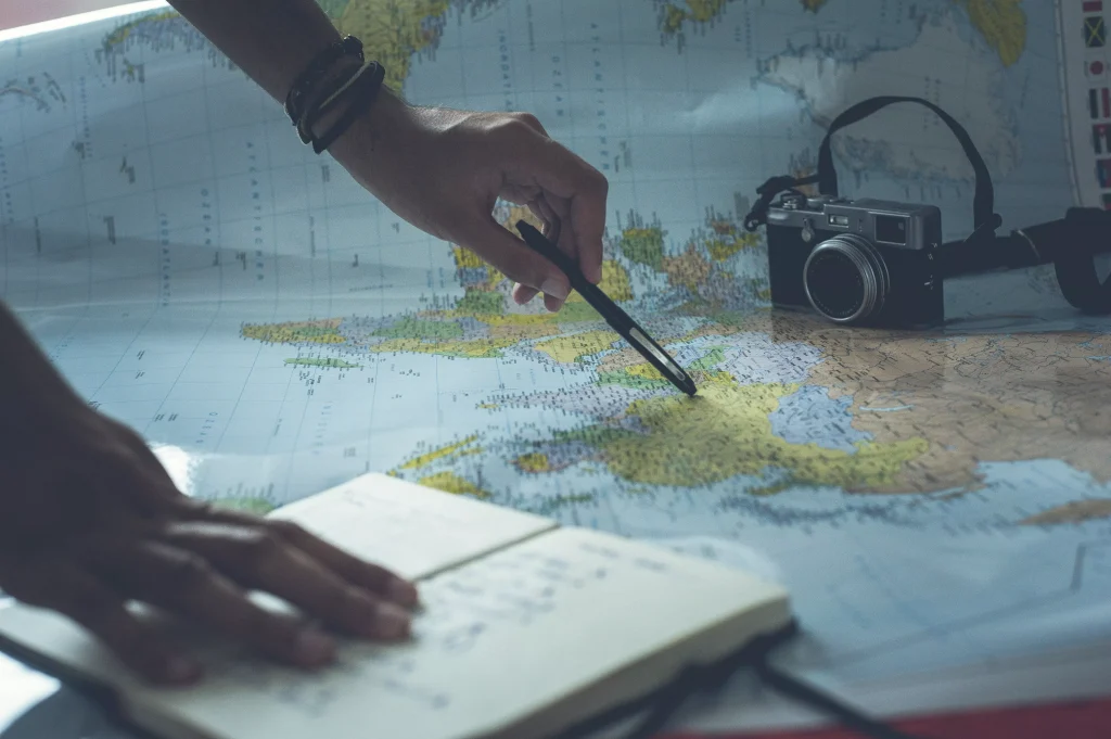 Map with a camera and a notebook and a someone pointing on the map with a pencil