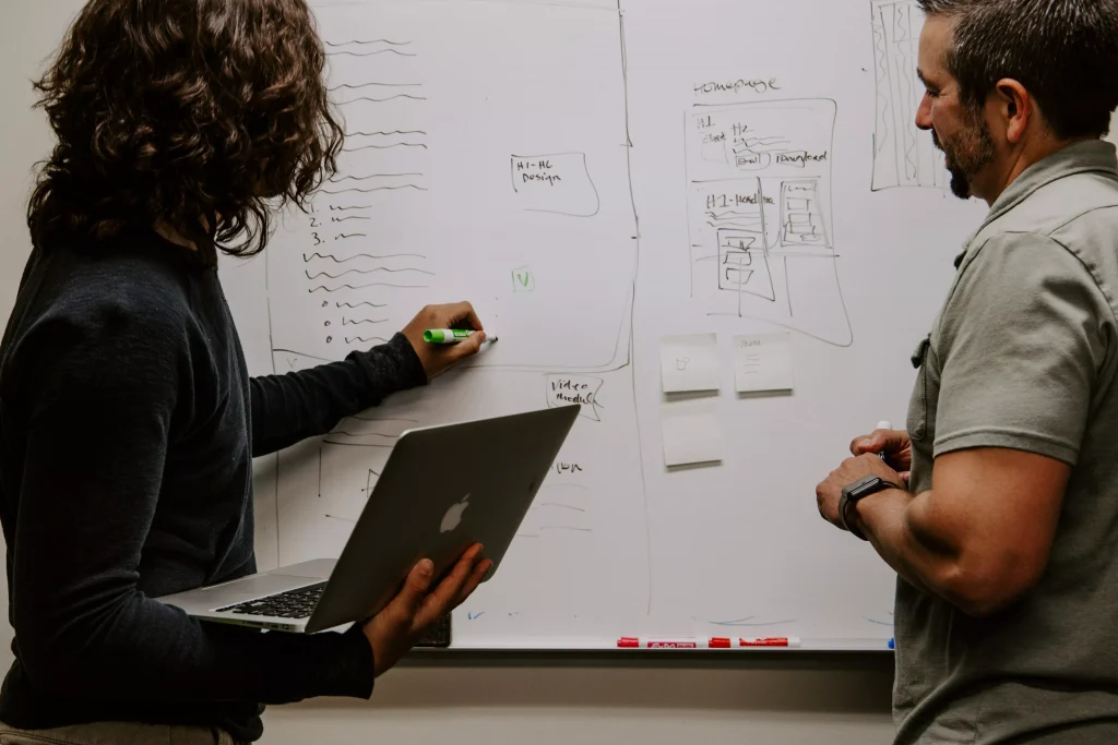 A man and a women writing something on a whiteboard and talking, making plans