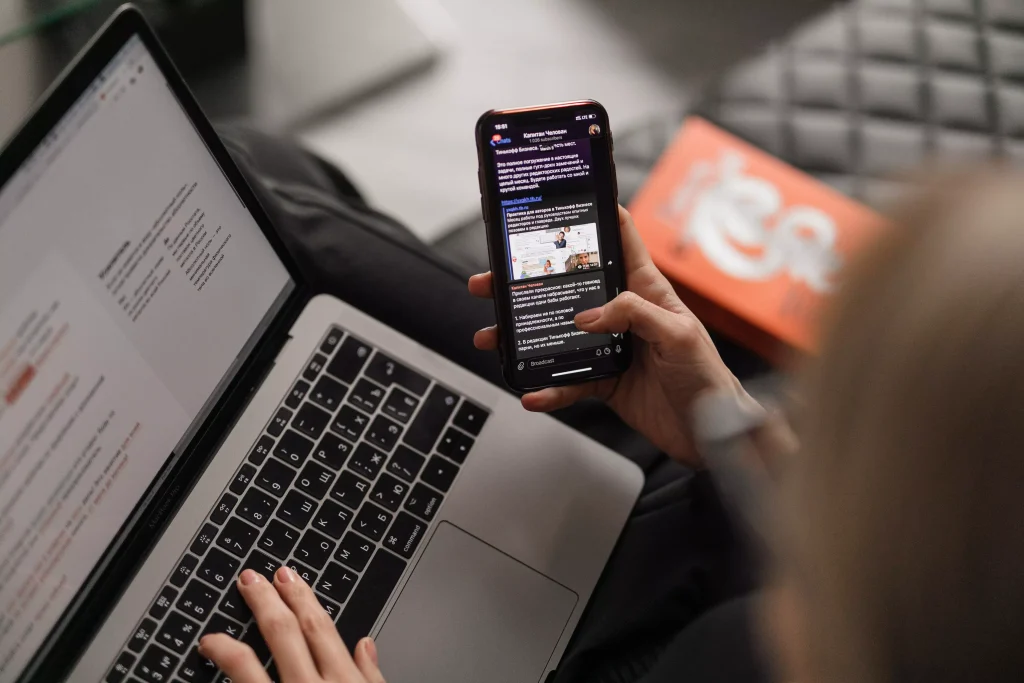 A laptop and phone used by a person at the same time