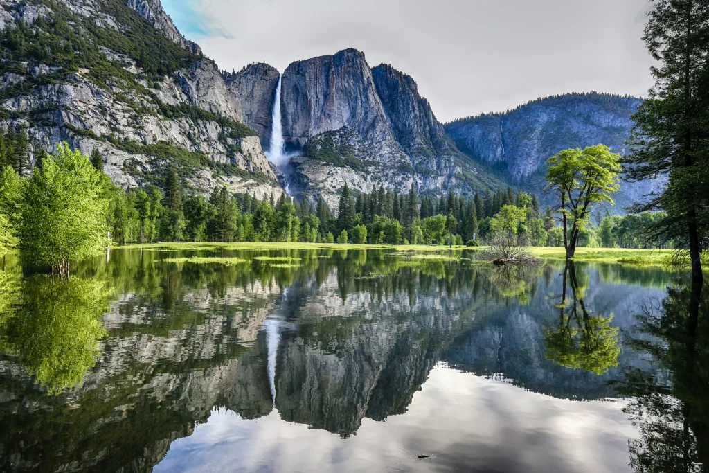 clear water surrounded by green trees fields and big mountains