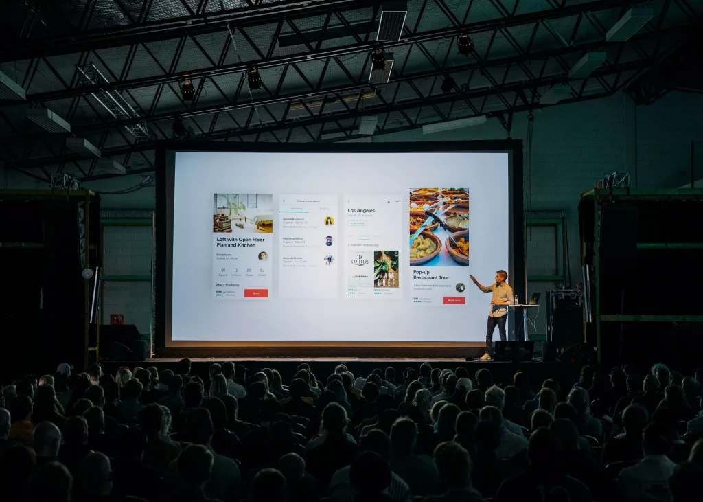 A guy is presenting something to a larger group of people on a big screen