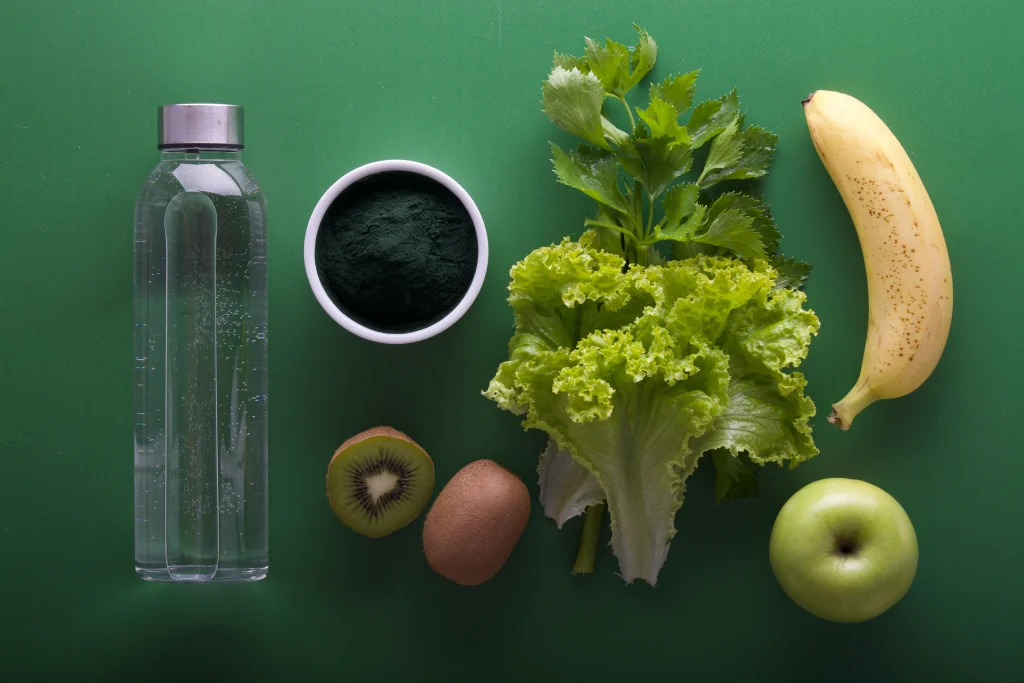 Fruits and vegetables placed ona desk next to a glass botel of water