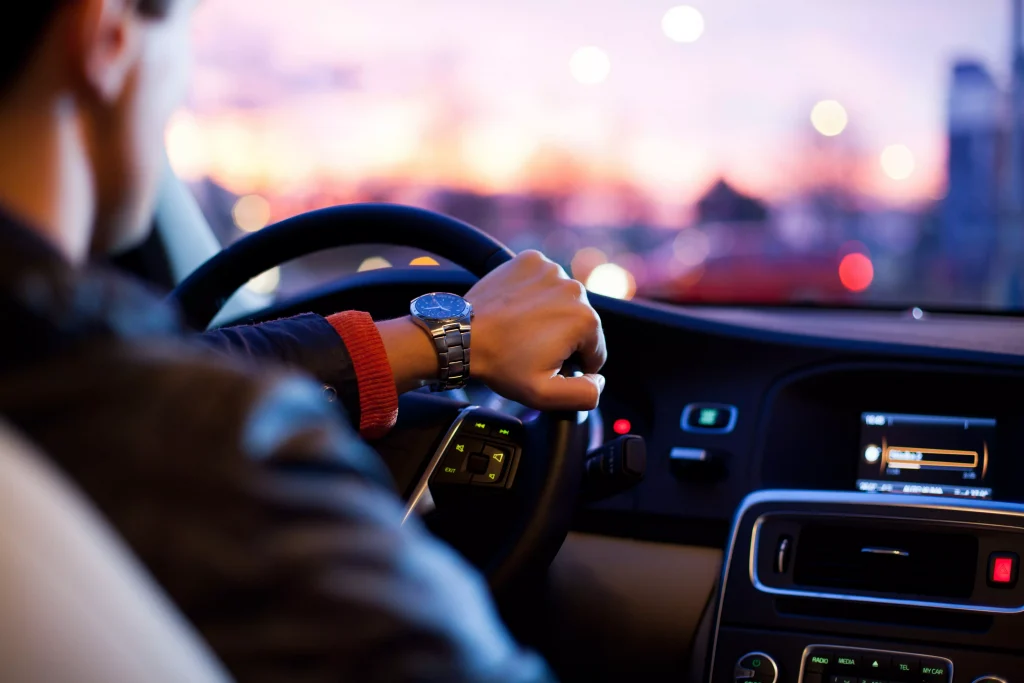 A man with a watch on the left hand steering a wheel of a car