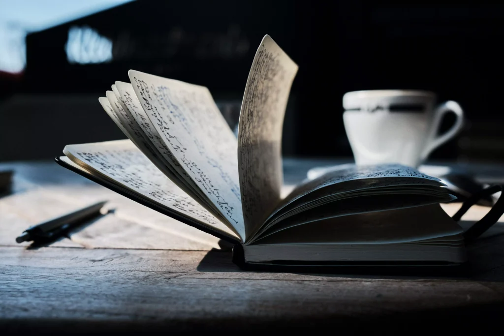 A journal with some notes written in it. Next to the journal there is a pen and a coffe cup