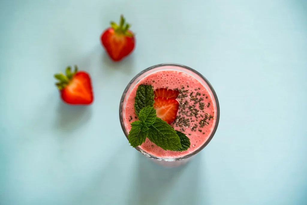 A smoothie with berries next to a sliced strawberry