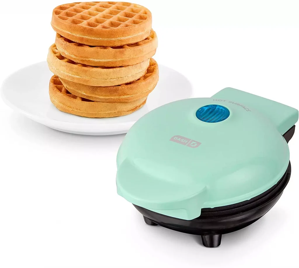 a light blue waffle maker next to some waffles