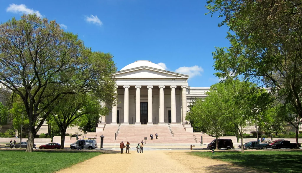 a white building on a grass between trees and a group of people