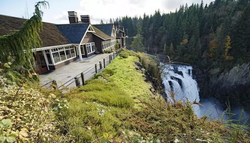 a beautfiul brown house with white windows next to a waterfall