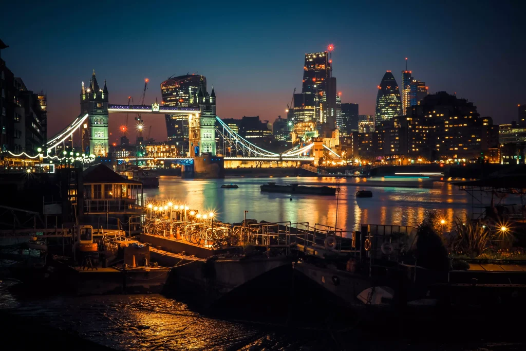 a bridge with a lot of lights above a river next to some buildings