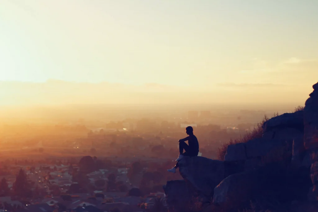 man sitting on a cliff above a town 