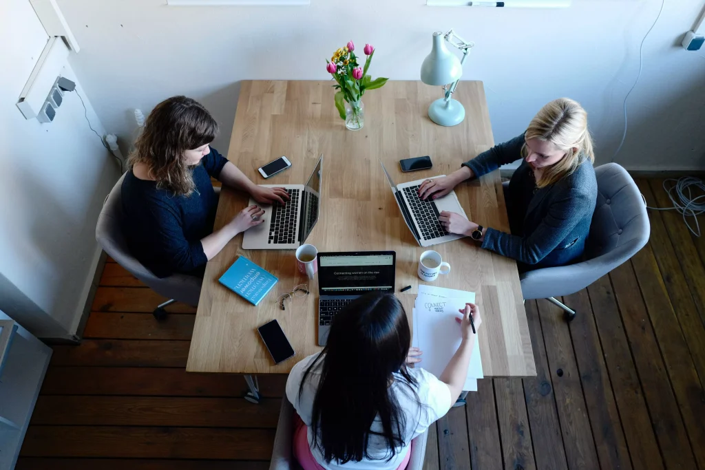 three girls siting at a table looking at laptops