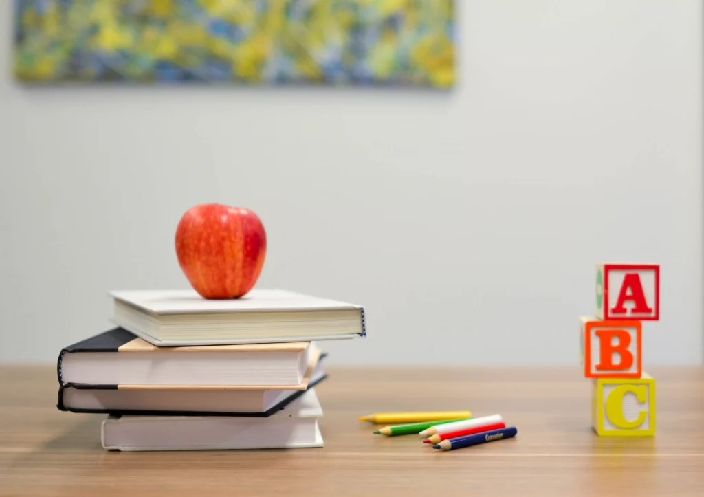 red apple on books next to some pens