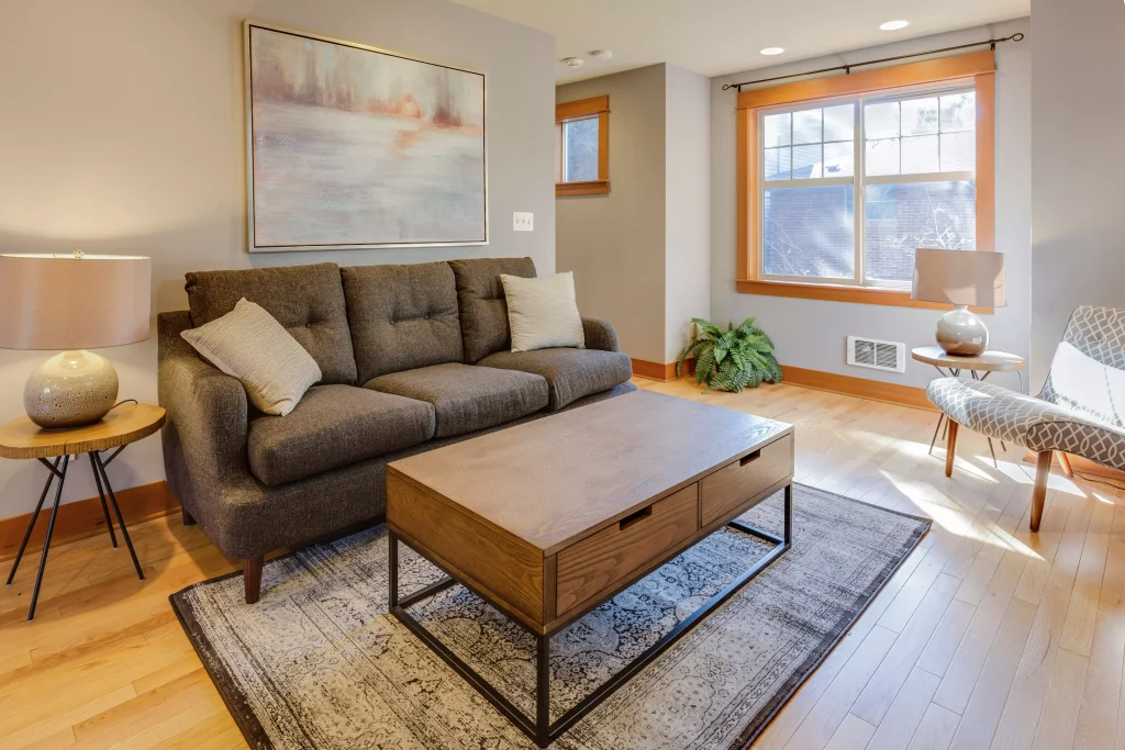 a minimalistic living room with a dark couch with white pillows on it and a brown table