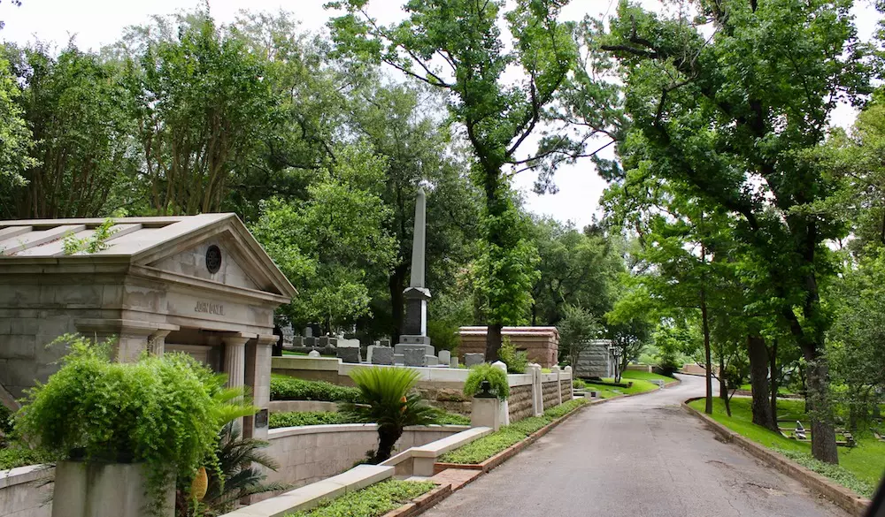 a road in a park with green trees and stone structures