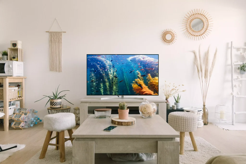 a big tv next to a grey table and little white chairs