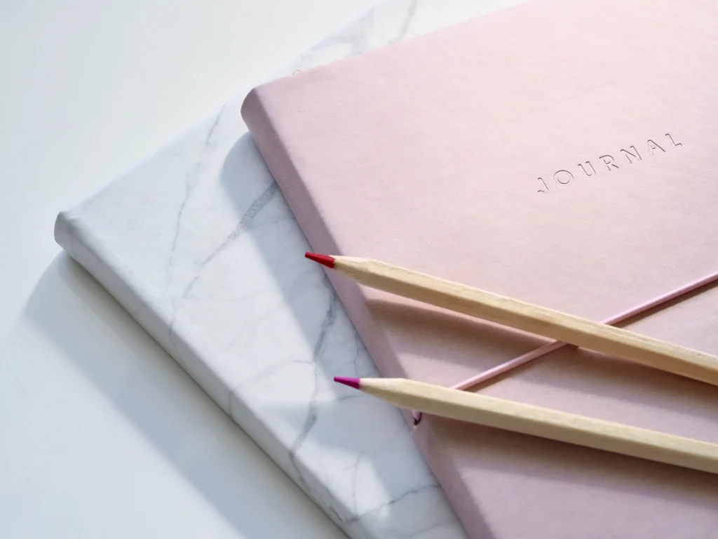 two journals one white one pink with two pencils