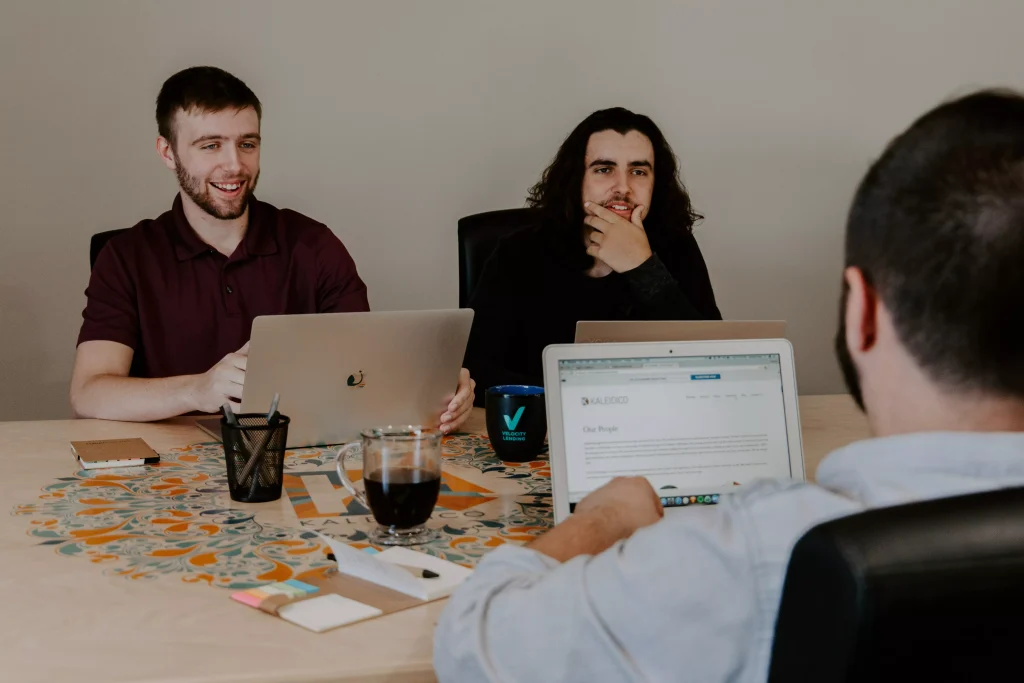 three guys with laptops speaking to each other