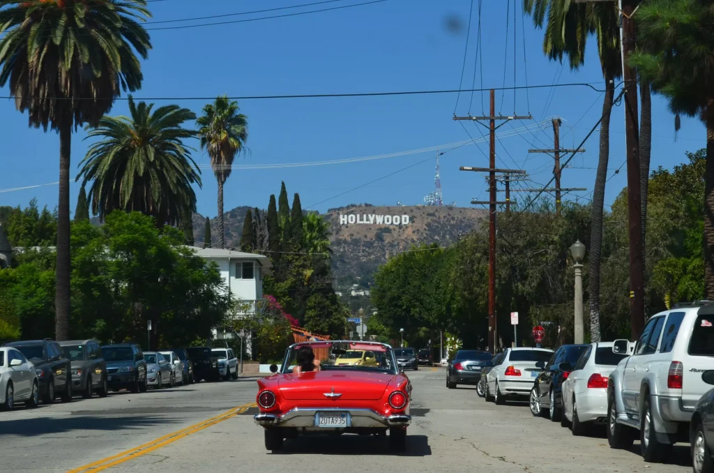 a red cabriolet car driving through a street with palm trees