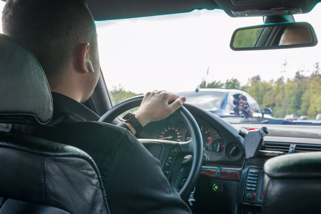 man driving a car in day photohgraphed from the backseat