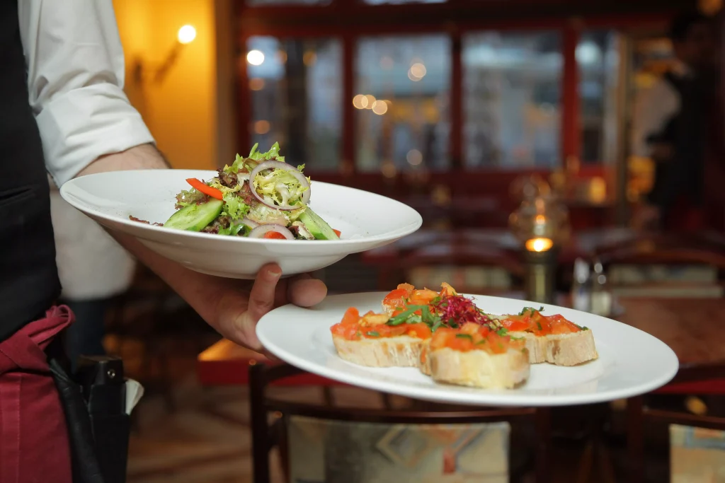 a bartender holding two white porculan plates full of food in a restaurant