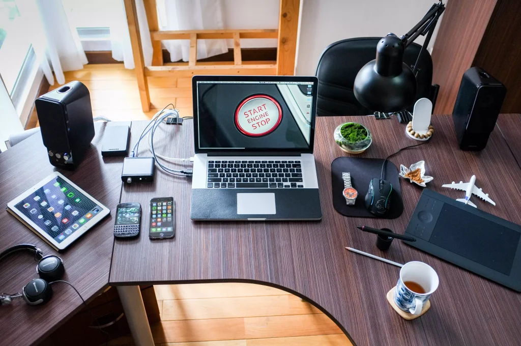 laptop on a office table next to a lot of electronic gadgets