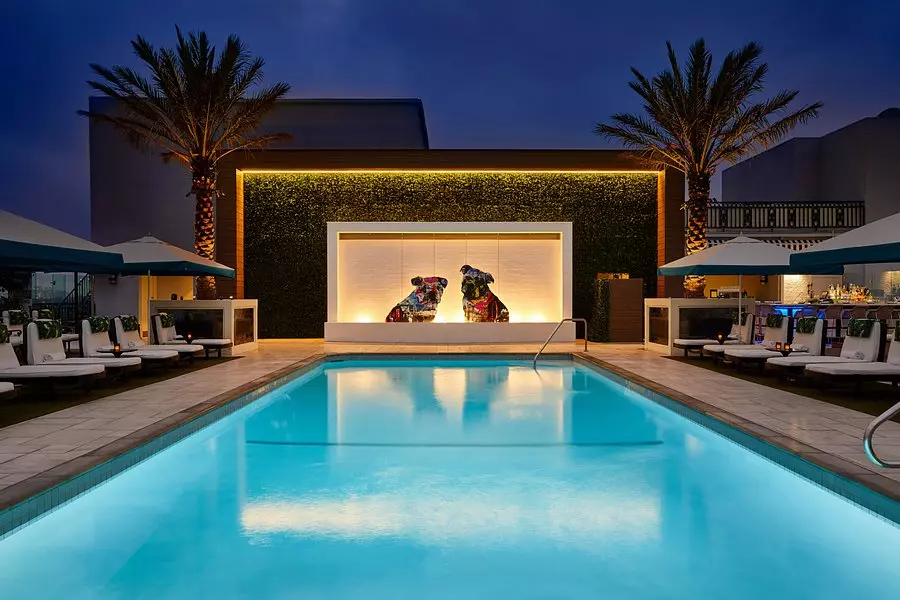 a pool with palm trees and statues in the back photographed at night