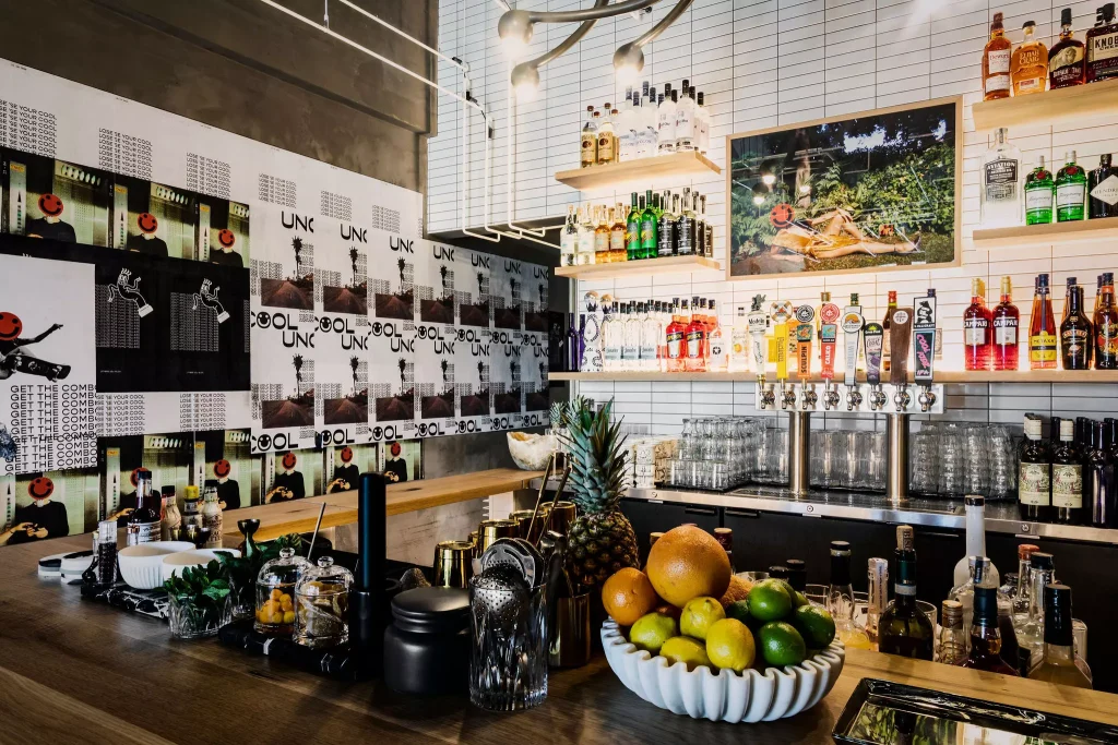 an organized bar with a lot of drinks and a bowl of fruits 