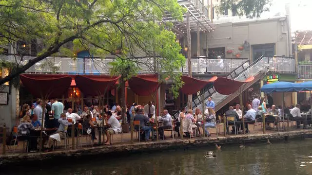 people sitting outside of a restaurant near the river