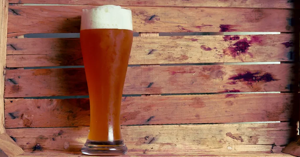 a full glass of beer infront of a wooden structure