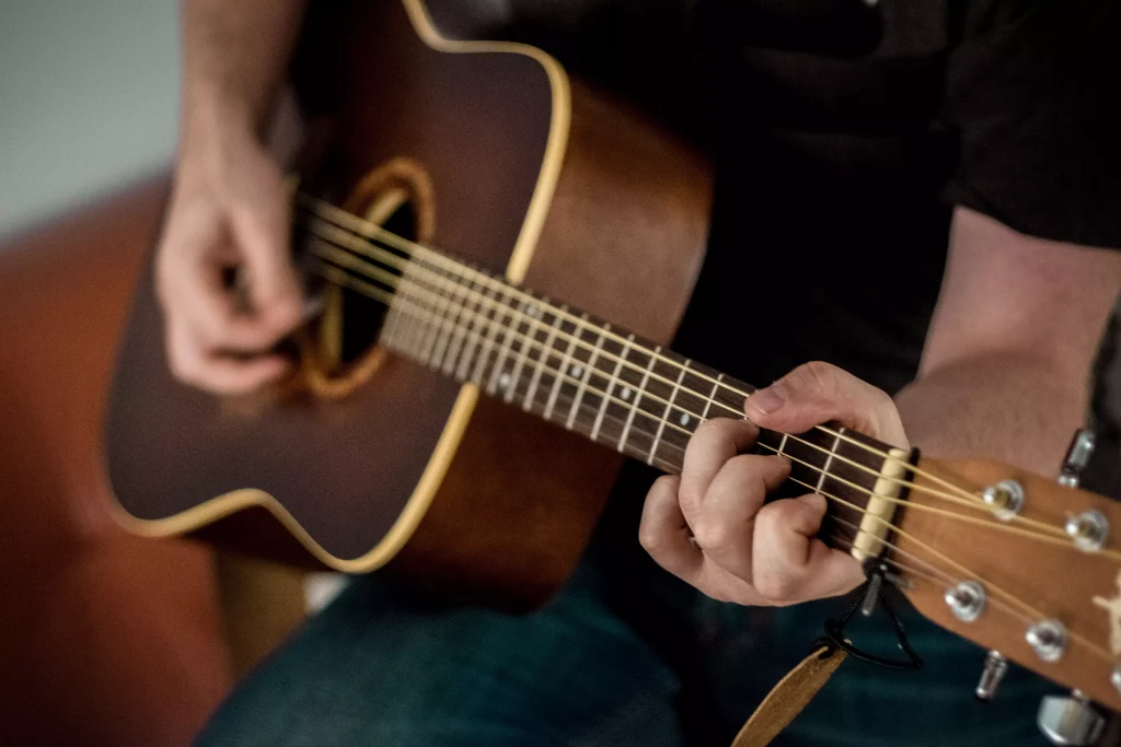 a guy in jeans playing a brown acoustic guitar