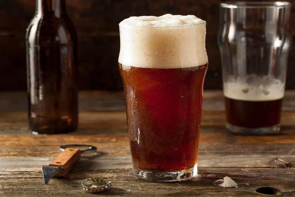 a full glass of brown beer next to a beer bottle and an empty glass