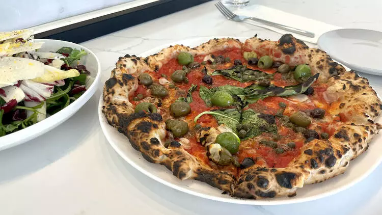 a pizza on a white plate next to some other food