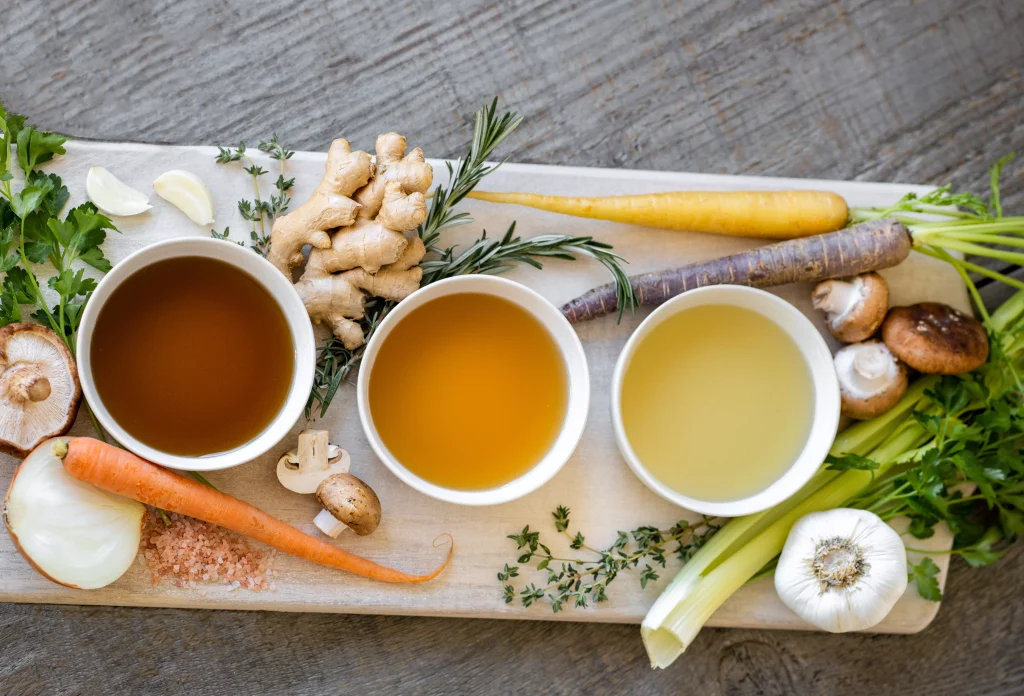 three small bowls of soup on a white square plate full of fresh vegetables