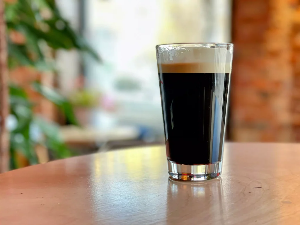 a small glass almost full of dark color beer