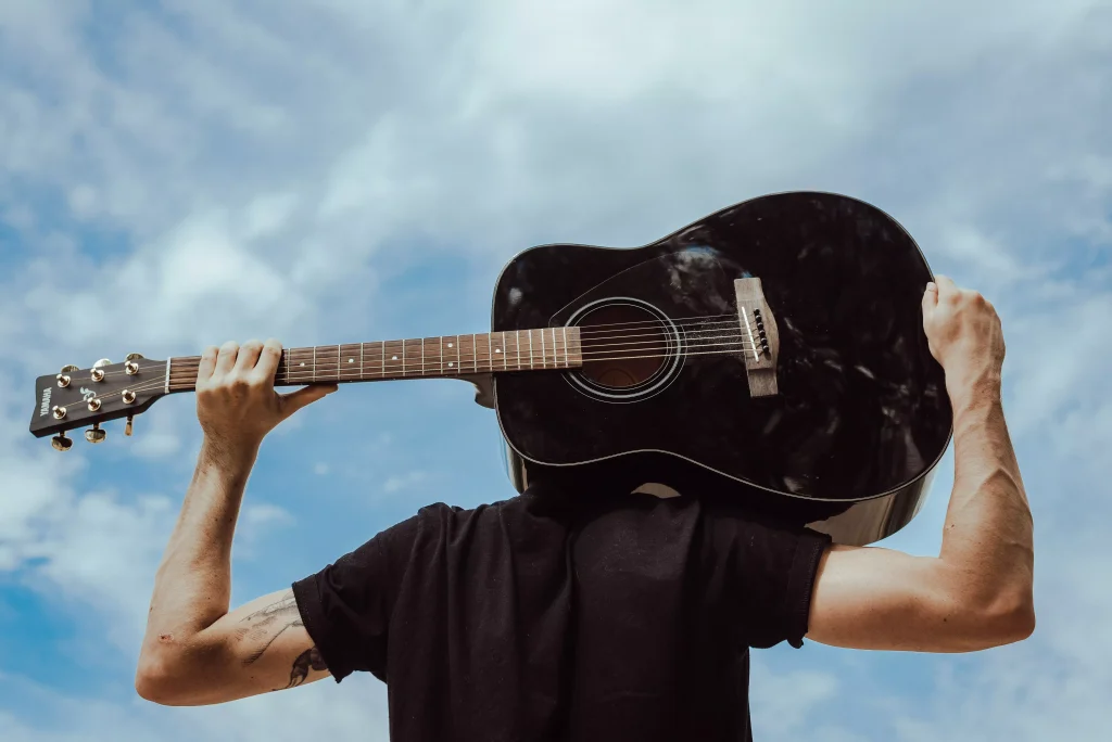 a person in a black shirt holding a black color guitar behind his head