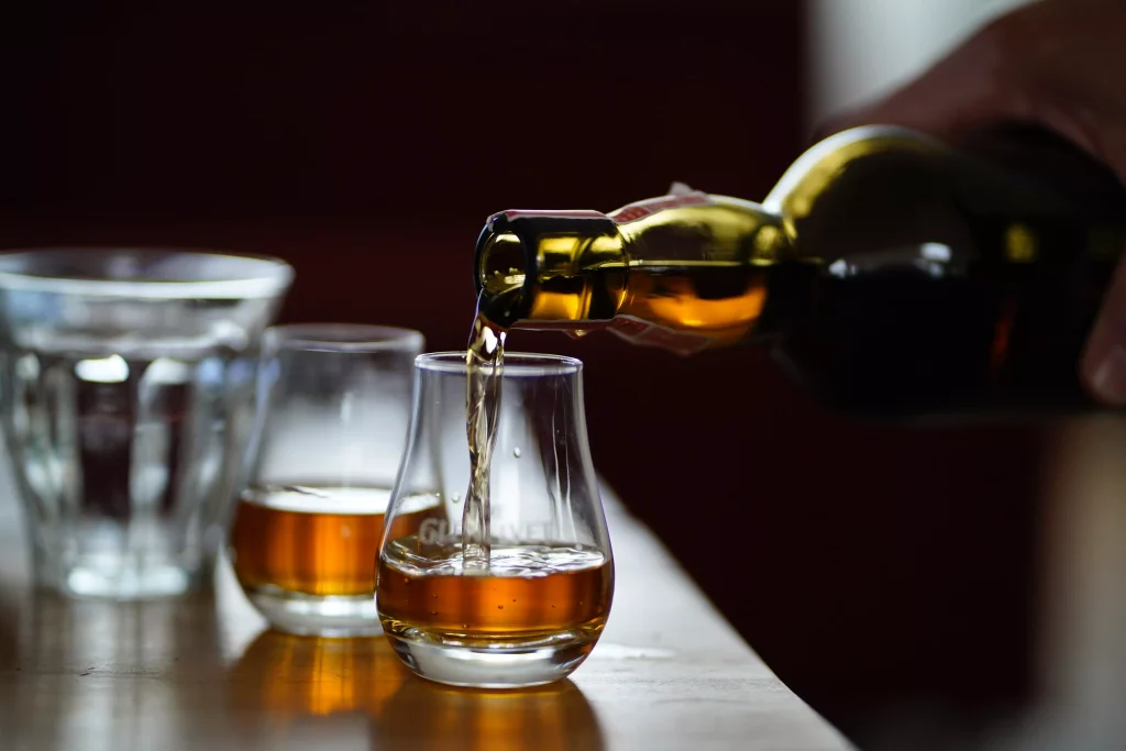 a person pouring a drink from a bottle in small glasses