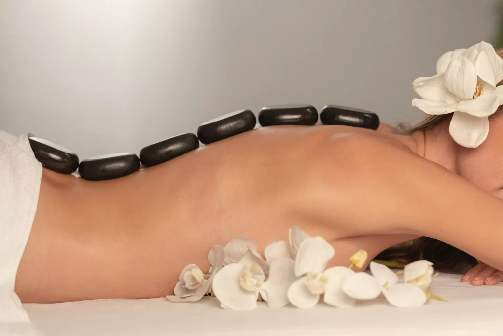 women with a flower in her hair and massage stones on her back