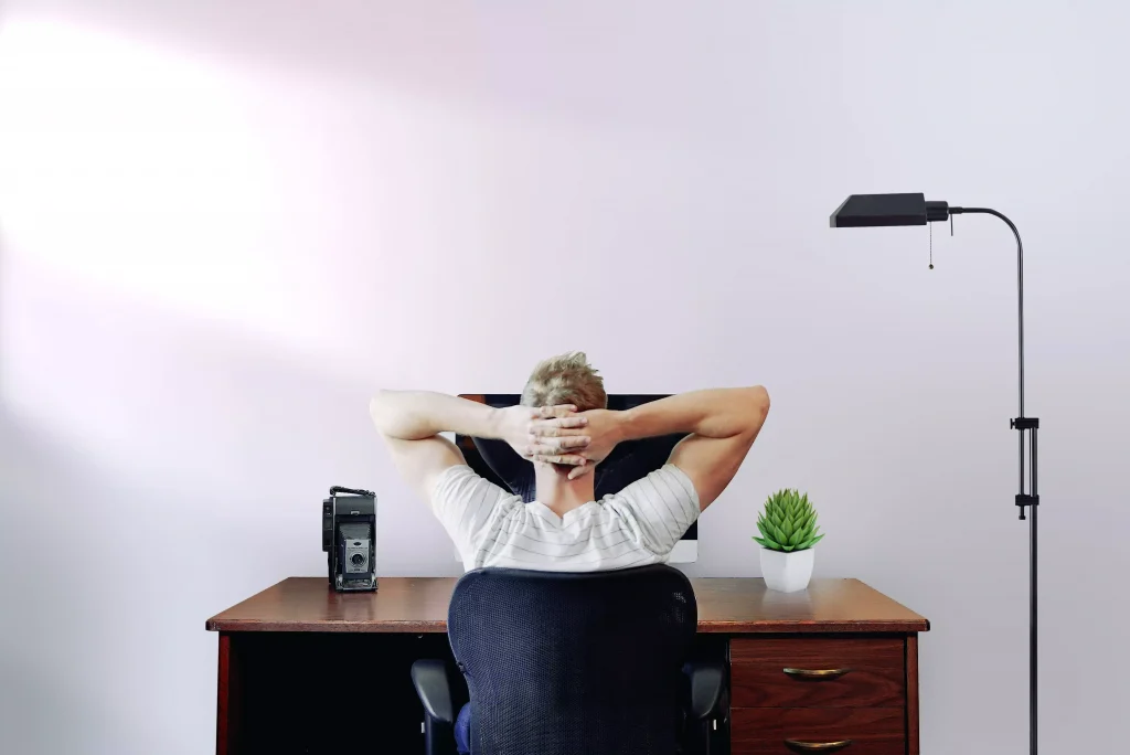 a guy sitting at a desk with his hands behind his head