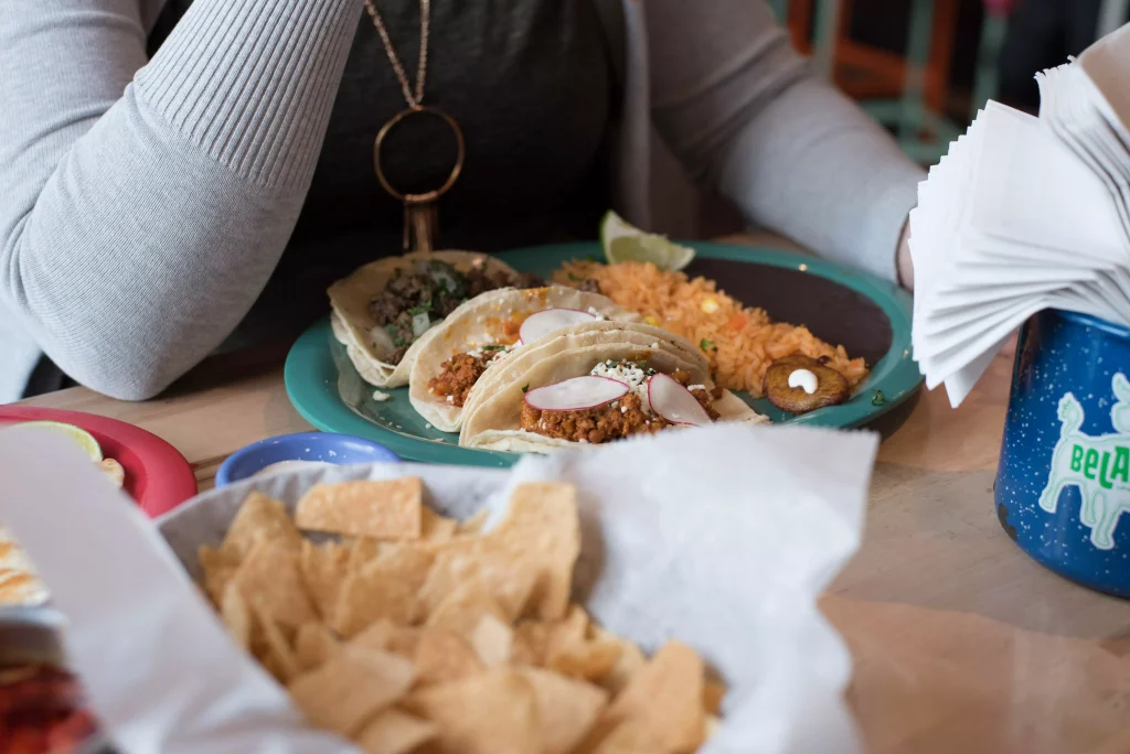 a women in a grey shirt eating tacos in a restaurant