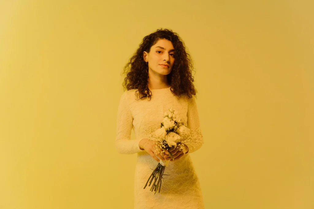 a women with curly hair holding flowers infront of a yellow background