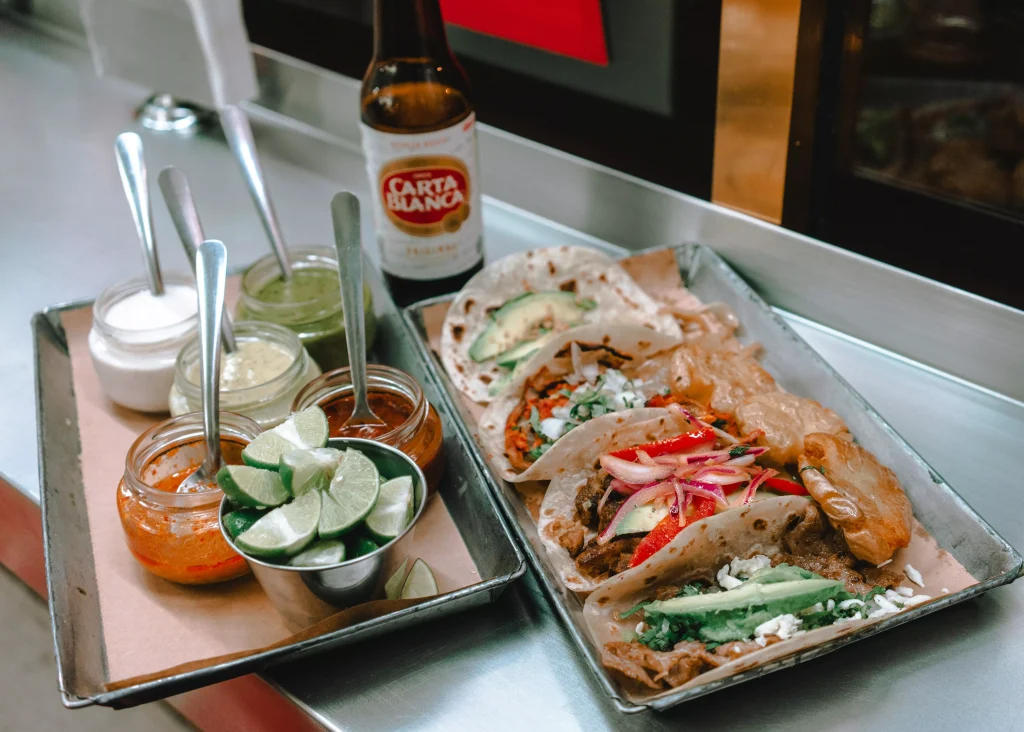 two square plates of tacos and salads next to a brown bottle of beer