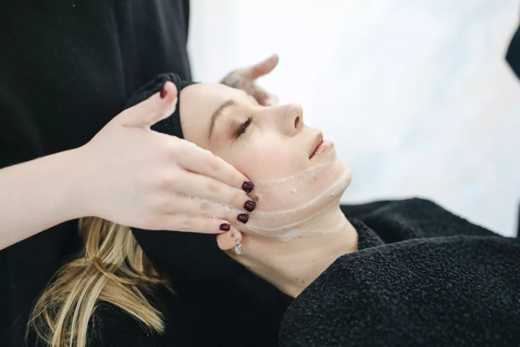 women with black color nails applying face cream to antoher women with black color headband