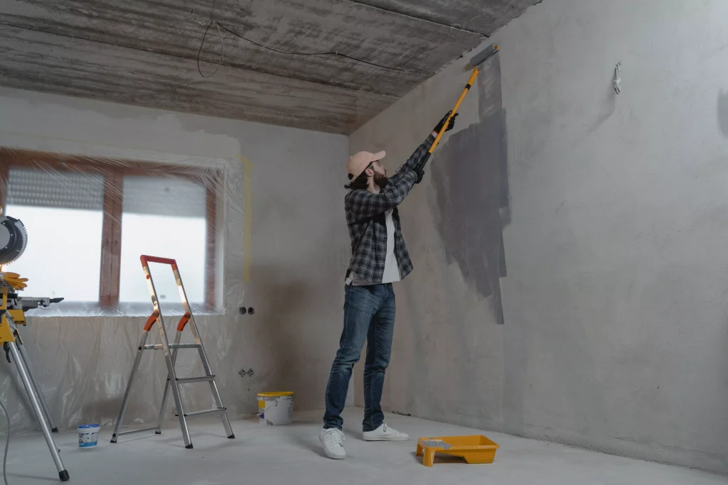 a man in a grey shirt and white cap paining a wall in grey