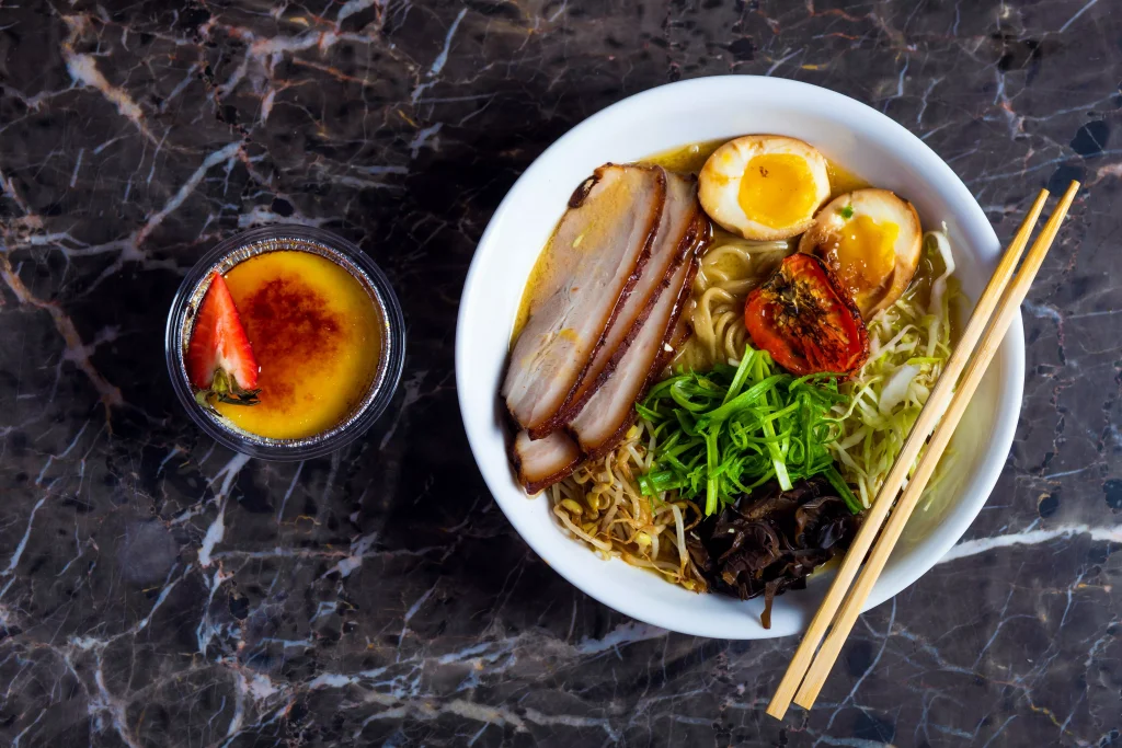 pork eggs and pasta in a white bowl next to a smaller glass bowl